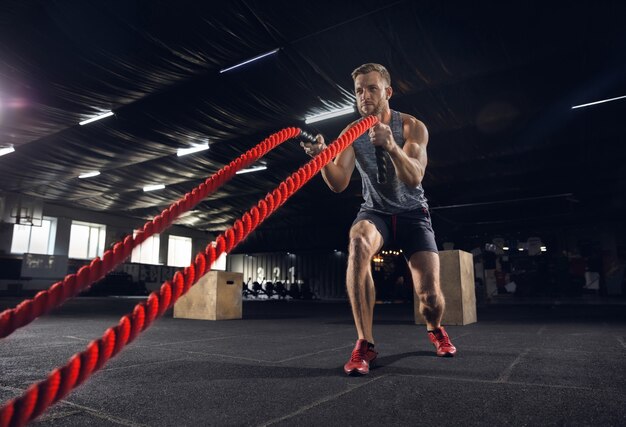 Giovane uomo in buona salute, atleta che fa esercizio con le corde in palestra. Unico modello maschile che pratica duramente e allena la parte superiore del corpo. Concetto di stile di vita sano, sport, fitness, bodybuilding, benessere.