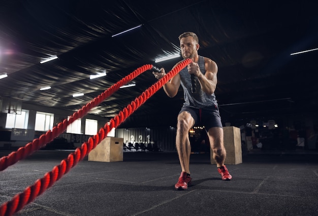 Giovane uomo in buona salute, atleta che fa esercizio con le corde in palestra. Unico modello maschile che pratica duramente e allena la parte superiore del corpo. Concetto di stile di vita sano, sport, fitness, bodybuilding, benessere.