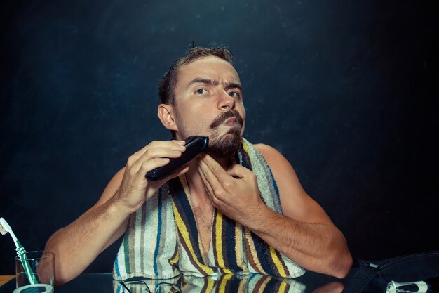 giovane uomo in camera da letto seduto davanti allo specchio grattandosi la barba a casa