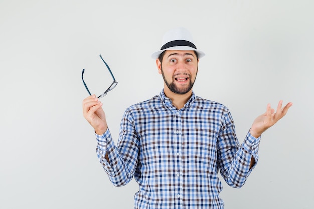 Giovane uomo in camicia a quadri, cappello con occhiali e guardando eccitato