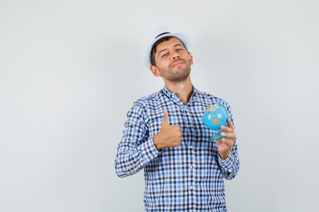 Giovane uomo in camicia a quadri, cappello tenendo il globo