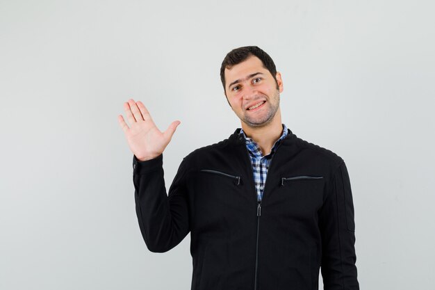 Giovane uomo in camicia, giacca agitando la mano per salutare e guardando allegro