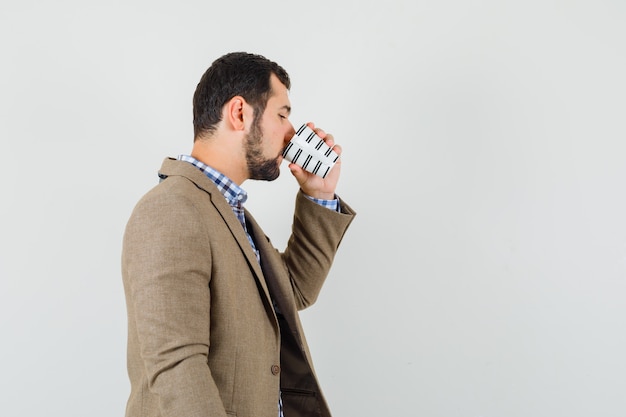 Giovane uomo in camicia, giacca, bere caffè e guardando pensieroso.