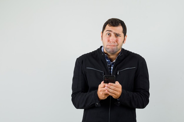 Giovane uomo in camicia, giacca che tiene il telefono cellulare e sembra impotente.