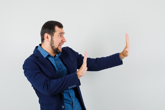 Giovane uomo in camicia, giacca che tiene le mani in modo protettivo e sembra spaventato.