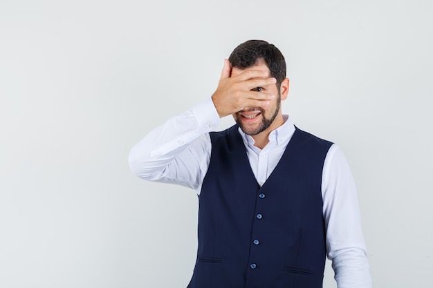 Giovane uomo in camicia, gilet guardando attraverso le dita e guardando curioso