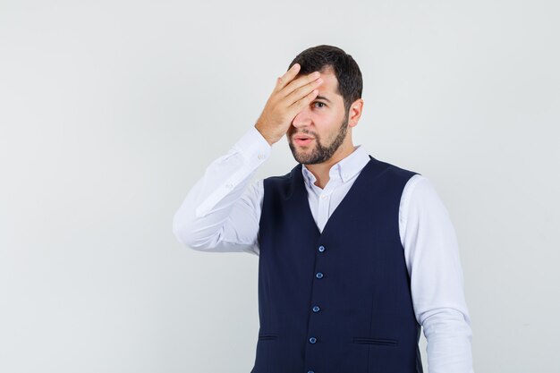 Giovane uomo in camicia, giubbotto tenendo la mano sull'occhio