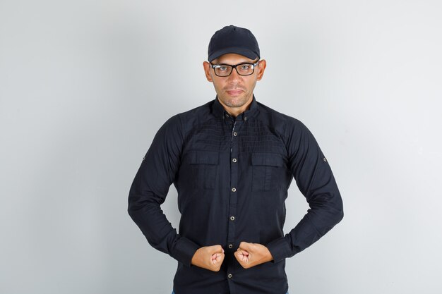 Giovane uomo in camicia nera con cappuccio, occhiali stringendo i pugni e guardando fiducioso