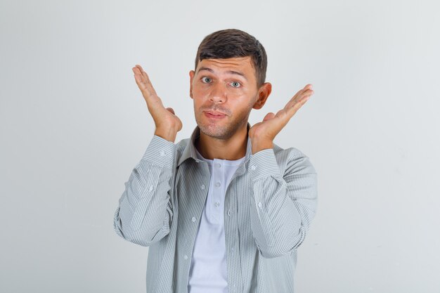 Giovane uomo in camicia tenendo le palme aperte vicino al viso