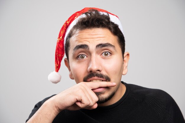 Giovane uomo in cappello di Babbo Natale che morde il dito.