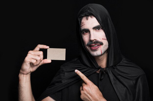 Giovane uomo in costume di Halloween in posa in studio con un piccolo pezzo di carta