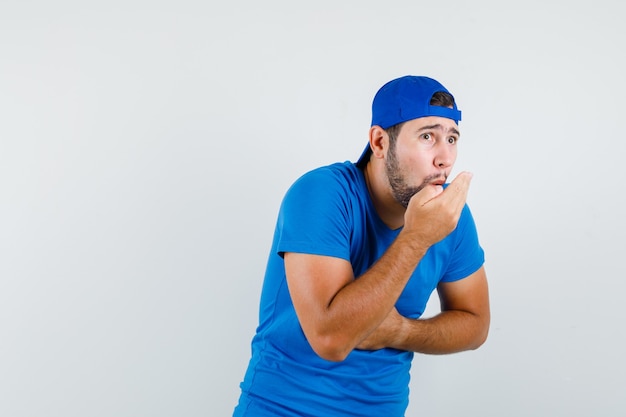 Giovane uomo in maglietta blu e berretto che fischia trattenendo il respiro