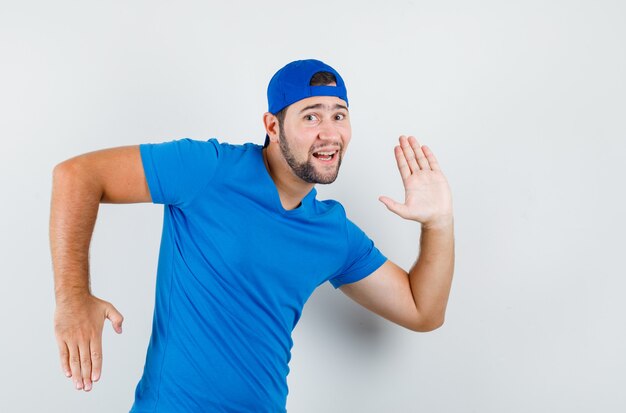 Giovane uomo in maglietta blu e berretto gesticolando come fare movimento e sembrare divertente