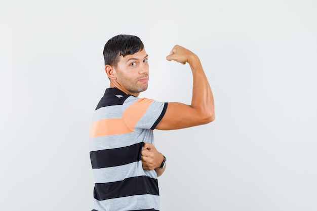 Giovane uomo in maglietta che mostra i muscoli del braccio e che sembra forte