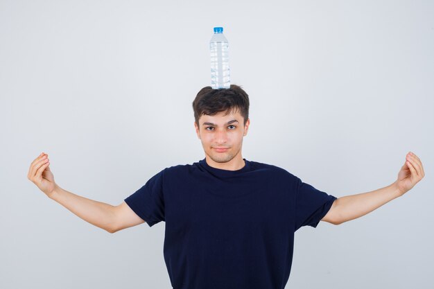 Giovane uomo in maglietta nera che tiene una bottiglia d'acqua sulla testa, facendo gesto italiano e guardando fiducioso, vista frontale.