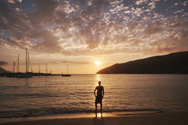 Giovane uomo in piedi di fronte al mare nell'isola di Amorgos, Grecia al tramonto