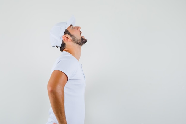 Giovane uomo in t-shirt, cappello alzando lo sguardo e guardando turbato, vista frontale. spazio libero per il testo