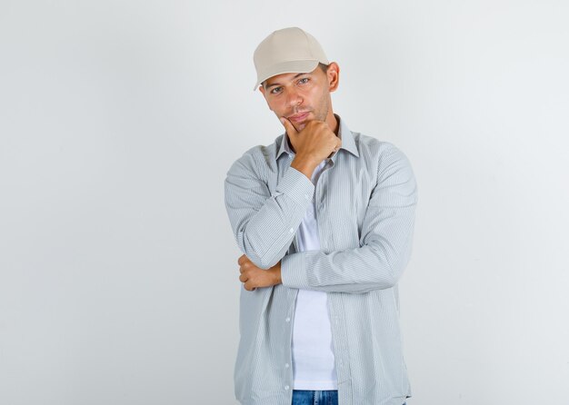 Giovane uomo in t-shirt con cappuccio, jeans in piedi con la mano sul mento