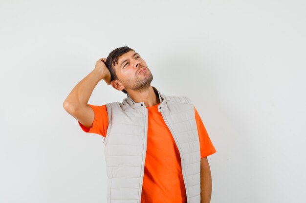 Giovane uomo in t-shirt, giacca grattarsi la testa mentre cerca e guarda pensieroso, vista frontale