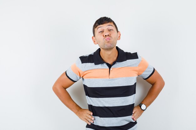 Giovane uomo in t-shirt imbronciato labbra con le mani sulla vita e guardando allegro