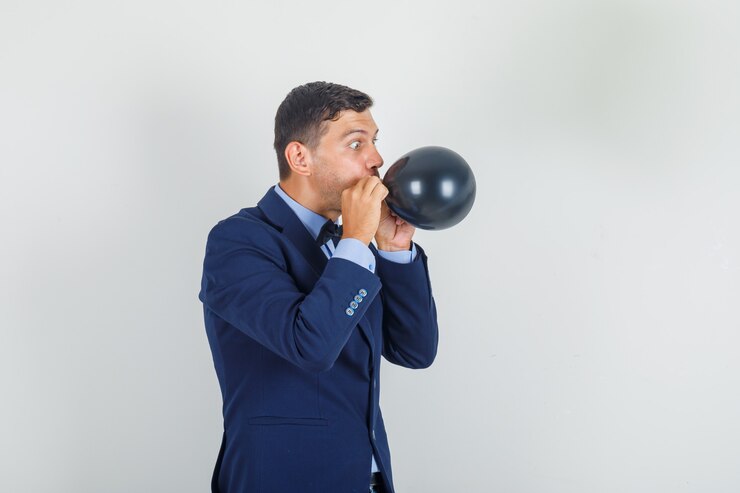 Foto gratuito giovane uomo in tuta che soffia palloncino nero