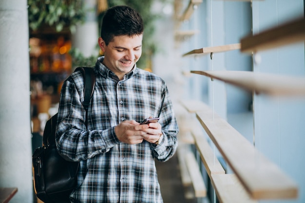 Giovane uomo in un caffè in piedi byy la finestra e parlare al telefono