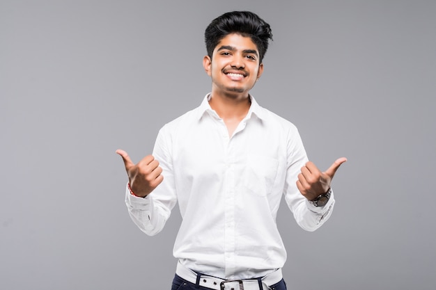 Giovane uomo indiano che controlla parete grigia isolata che approva facendo gesto positivo con la mano, pollici su che sorridono e felici per successo