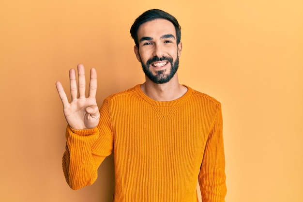 Giovane uomo ispanico che indossa abiti casual mostrando e puntando verso l'alto con le dita numero quattro mentre sorride fiducioso e felice