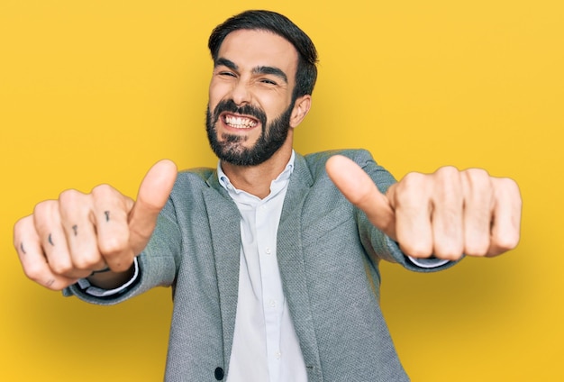 Giovane uomo ispanico che indossa abiti da lavoro che approva facendo un gesto positivo con il pollice in alto sorridente e felice per il gesto del vincitore di successo