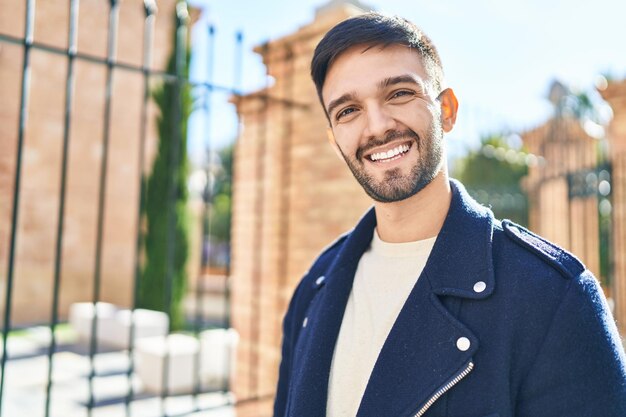 Giovane uomo ispanico sorridente fiducioso in piedi in strada