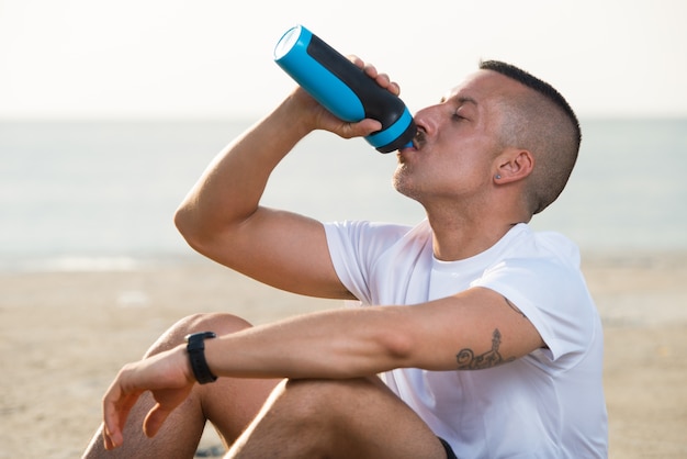 Giovane uomo rilassato che beve acqua dalla bottiglia