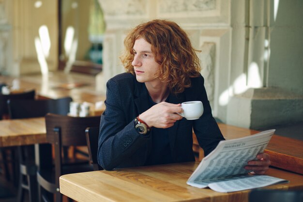 Giovane uomo rossastro che beve caffè mentre guardando a destra