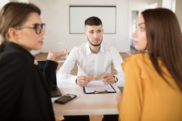 Giovane uomo sconvolto in camicia bianca che guarda tristemente i datori di lavoro mentre trascorre del tempo in un ufficio moderno Candidato maschio in attesa dei risultati del colloquio di lavoro