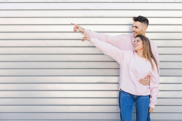 Giovane uomo sorridente che abbraccia attraente donna felice con le mani a lato