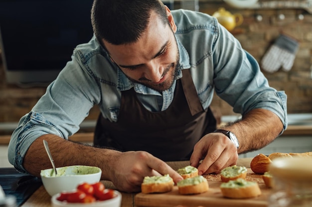 Giovane uomo sorridente che prepara la bruschetta di avocado in cucina.