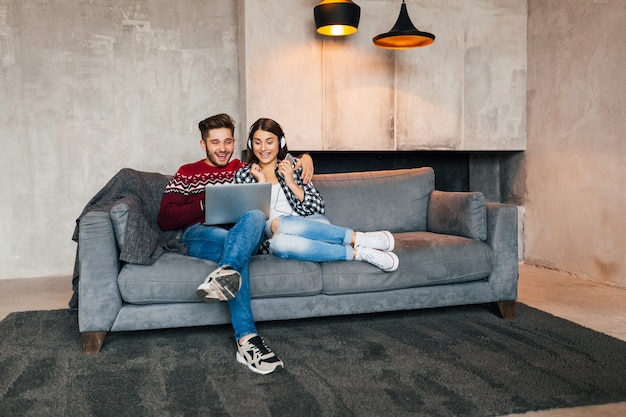 Giovane uomo sorridente e donna seduta a casa in inverno guardando nel computer portatile con l'espressione del viso uscito sorpreso, utilizzando internet, coppia nel tempo libero insieme, emozione felice e positiva