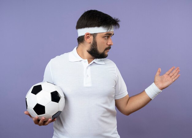 Giovane uomo sportivo guardando al lato che indossa la fascia e il braccialetto tenendo palla e tenendo la mano a lato