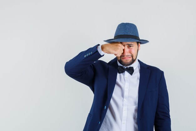 Giovane uomo strofinando gli occhi mentre piangeva in tuta, vista frontale del cappello.