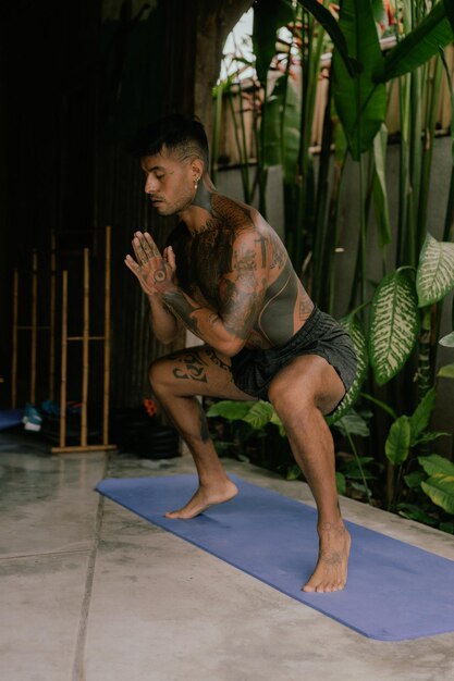 Giovane uomo tatuato latinoamericano pratica yoga all'aperto durante le vacanze di ritiro a Bali, stretching, meditazione, benessere