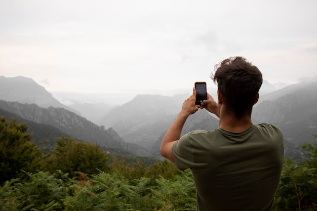 Giovane viaggiatore maschio che scatta una foto delle montagne con il suo smartphone