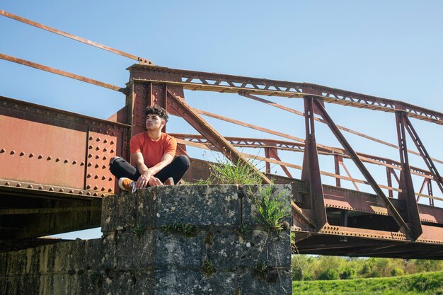 Giovane viandante maschio sola che si siede vicino al ponte