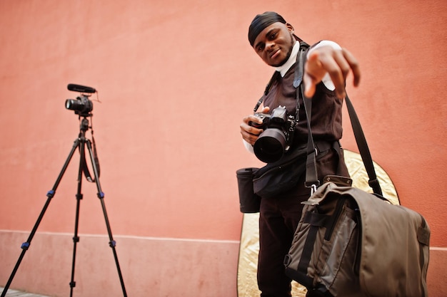 Giovane videografo afroamericano professionista che tiene una fotocamera professionale con attrezzatura professionale Cameraman afro che indossa un duraq nero che realizza un video