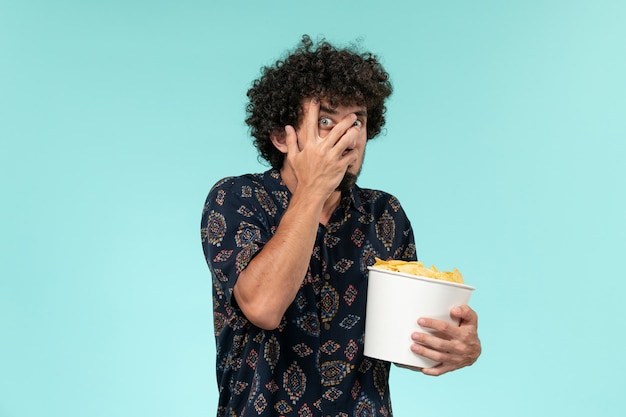 Giovane vista frontale che tiene il cestino con patatine fritte e guardare film sul teatro di film cinema maschio di film scrivania blu