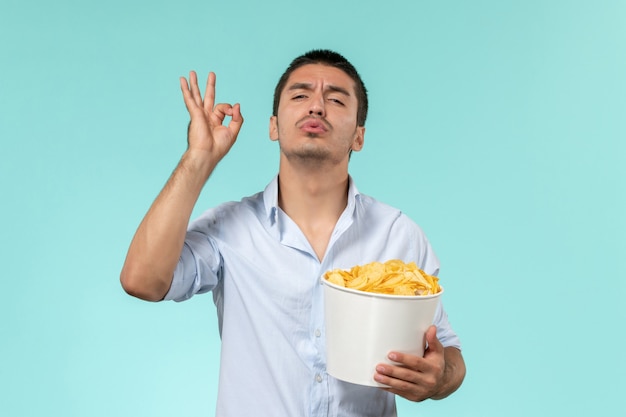 Giovane vista frontale che tiene patatine fritte in posa su un cinema maschio remoto solitario muro blu