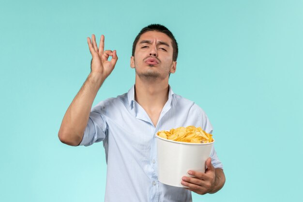 Giovane vista frontale che tiene patatine fritte in posa su un cinema maschio remoto solitario muro blu