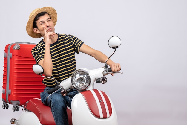 Giovane vista frontale con cappello di paglia sul ciclomotore pensando a qualcosa