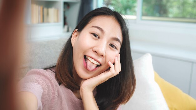 Giovane vlog asiatico della donna dell'adolescente a casa, femmina che per mezzo dello smartphone che fa video del vlog ai media sociali in salone. La donna di stile di vita si rilassa nel concetto di mattina a casa.