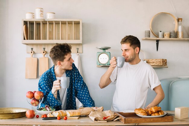 Giovani amici che godono bevendo caffè con frutta e pane sul bancone della cucina