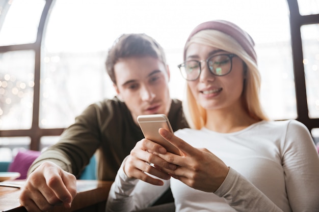 Giovani amici felici che si siedono in caffè mentre chiacchierano per telefono.