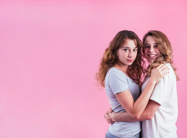 Giovani amici femminili sorridenti che si abbracciano contro fondo rosa